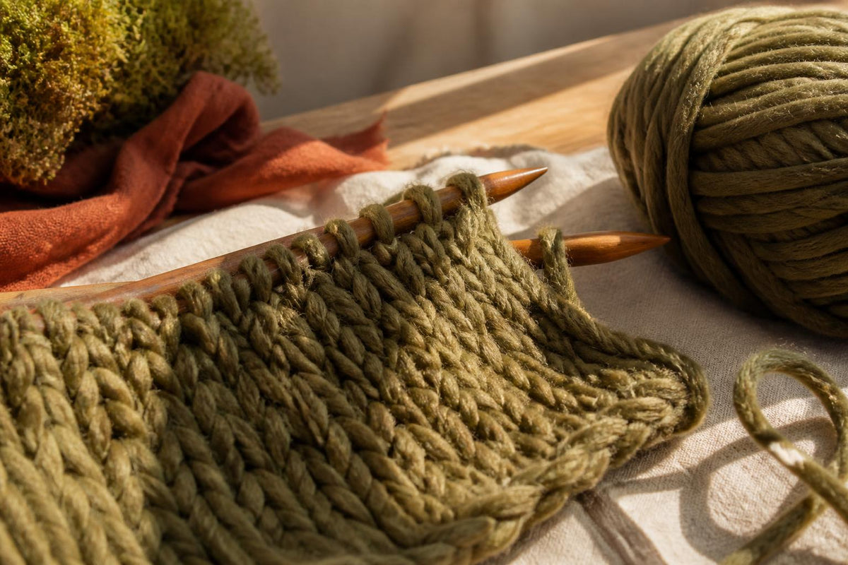 Close-up of thick, cream-colored wool yarn coiled neatly on a wooden surface next to silver knitting needles