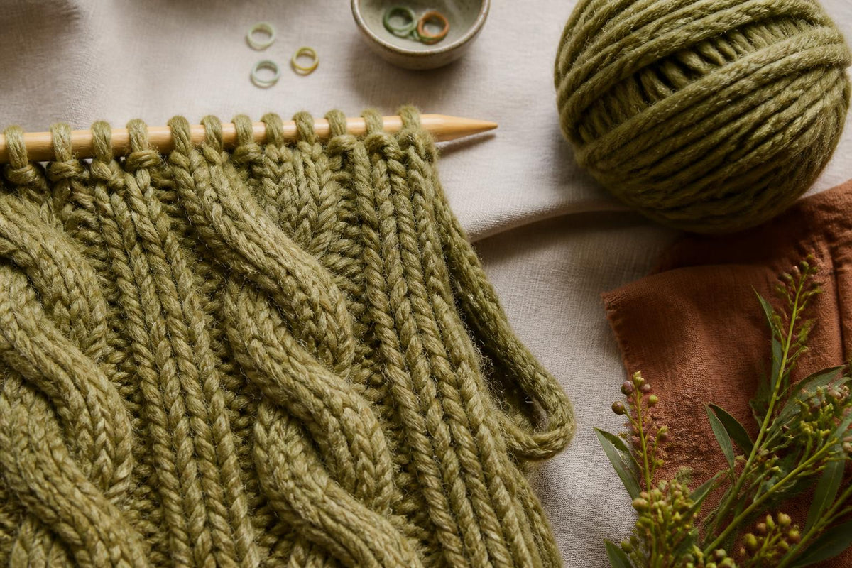 A stack of folded wool sweaters in varying colors and textures resting on a wooden table